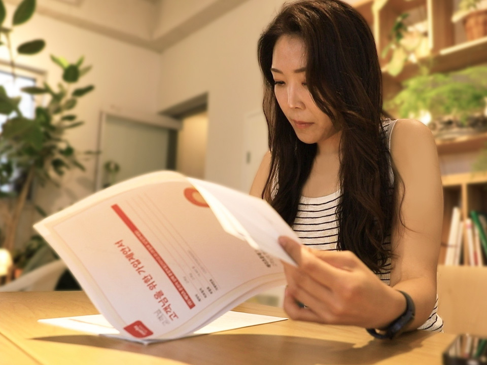 수익 구조, 수익 창출, 보험 수수료, 현실적인 부업, 실내 테이블에서 긴 웨이브 머리에 줄무늬 민소매 상의를 입은 여성이 '고객님을 위한 가입제안서' 서류를 손에 들고 신중하게 검토하고 있는 모습